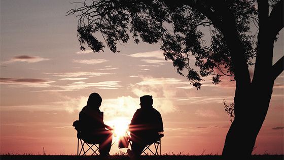 two people sitting outside in lawn chairs under a tree watching a sunset; image used for blog post about saving for retirement with your 401(k)
