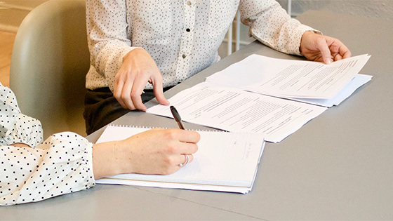 two women sitting at a table with various forms, one woman hands over a page and the other has pen in-hand to fill out paperwork; for a blog about not-for-profit board members information