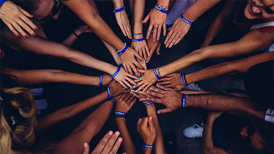 various arms extended to the center of the photo, with overlapping hands formed into a teamwork cheer; image used for a blog about executing a not-for-profit capital campaign
