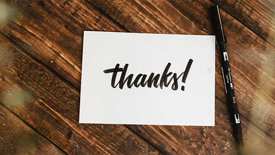a note card with the word "thanks" sits on a wooden table with a black marker; image used for blog post about not-for-profits acknowledging donor gifts