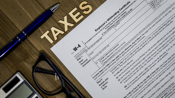 A photo of a W-4 tax form with a pen, calculator and reading glasses; image used for blog post about how to check if your withholding is adequate