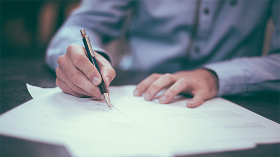 man in a blue button down shirt holds a pen to paper to sign documents; image used for blog post about not-for-profits regaining tax-exempt status