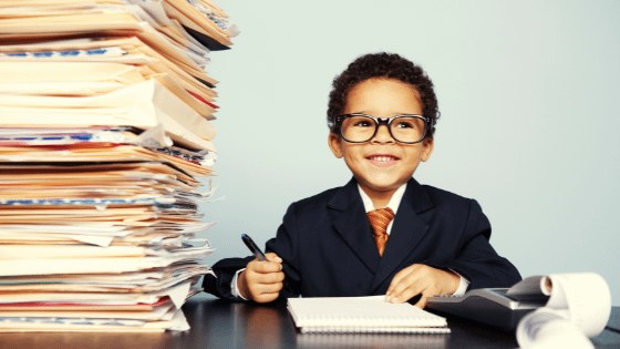 A photo of a child in a suit and tie and glasses sitting next to a stack of files; image used for blog post about kiddie tax