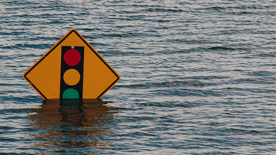 a golden yellow diamond street sign with red, yellow and green vertical circles, submerging below rising rain water, signifying tropical storm imelda in texas