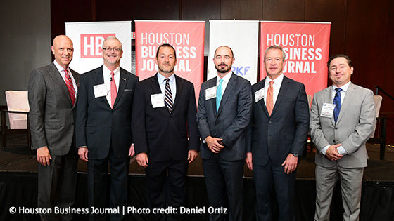 six American gentlemen standing in a line in front of tall posters for the Houston Business Journal and PKF Texas