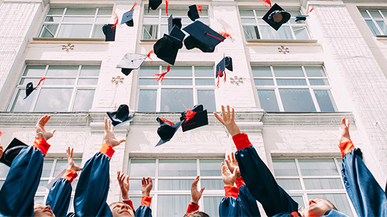 a group of students throwing their graduation caps in the air in front of a stone building with windows to celebrate available tax credits for higher education