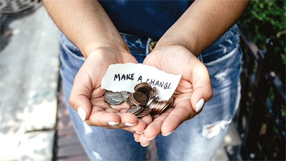 two hands cupped together, holding coins with a piece of paper saying "making a change," for a blog post about IRA Charitable Donations