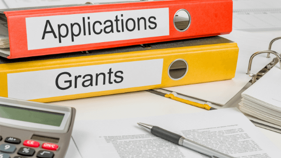 A photo of two binders labeled "Applications" and "Grants" on a table with a calculator, pen and financial documents; image used for blog post about tips for getting a not-for-profit grant