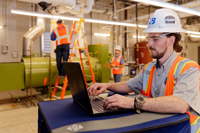 EAB engineer documenting building commissioning project details on a laptop