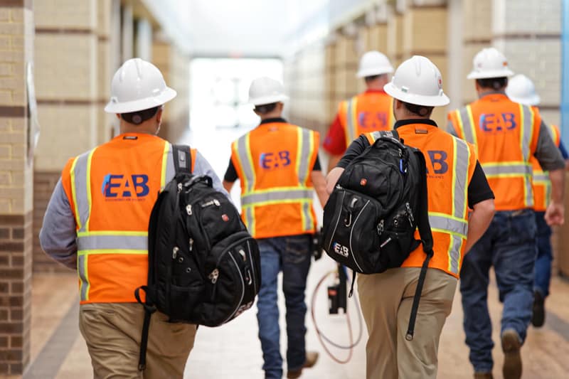 A group of commissioning engineers from Engineered Air Balance wearing high-visibility orange vests and white safety helmets