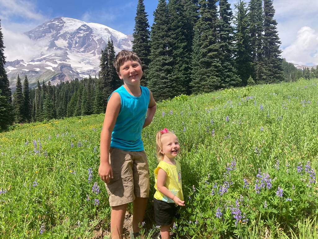 Kids standing in front of wildflowers and mountain at Mount Rainier National Park, a must see spot while camping in Washington