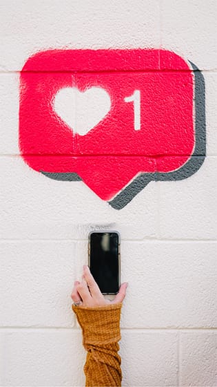 girl holding her iPhone towards a painted pink notification icon with a heart and 1; image used for blog post about not-for-profits working with social media influencers