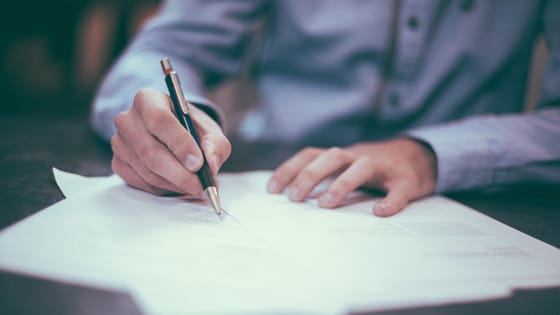 Image of a man in a blue shirt writing audit letters on pieces of paper with a pen