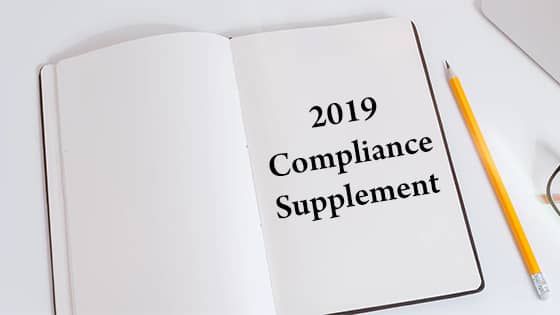 a pencil lying beside an open notebook with the printed words "2019 Compliance Supplement"