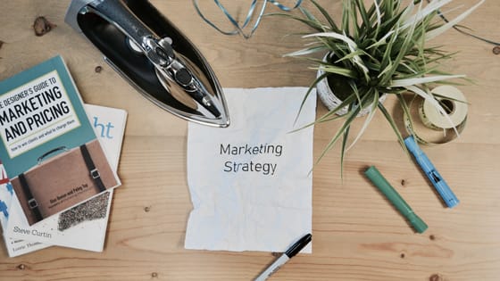 overhead view of a wooden desk with a piece of paper in the center that says "marketing strategy" with books sitting to the left, titled "marketing and pricing"