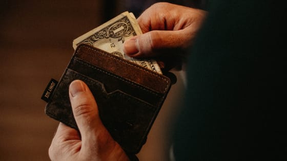 It would be smart to purchase items for your business now because of deprecation deductions with Section 179. This photo is of a person holding a leather wallet in one hand and pulling money out with the other.