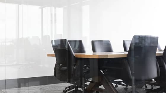 through a window, several black rolling chairs sit around a wooden table, a meeting room, maybe for FASB voting on delaying major standards