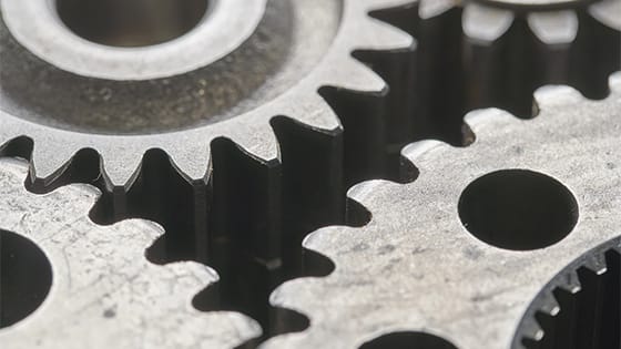 Silver metal gears turning, teeth fitting perfectly in each other; for a blog post about the greater houston partnership manufacturing industry forum