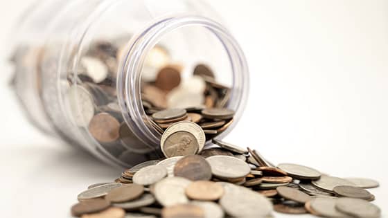 pennies, dimes, nickels and quarters spilling out of a clear glass jar; used for a blog post about saving on taxes with a 401(k) plan