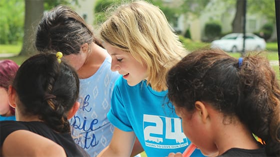 blonde woman in a turquoise shirt volunteering with multiple children; image used for a blog about not-for-profit corporate volunteers