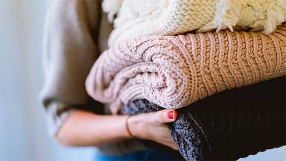 woman holding three knit sweaters; image used for blog post about tax implications on not-for-profit donors