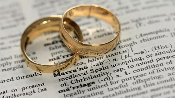 two gold wedding rings sitting on top of a dictionary defining "marriage;" image used for blog post about married couples filing tax returns separately