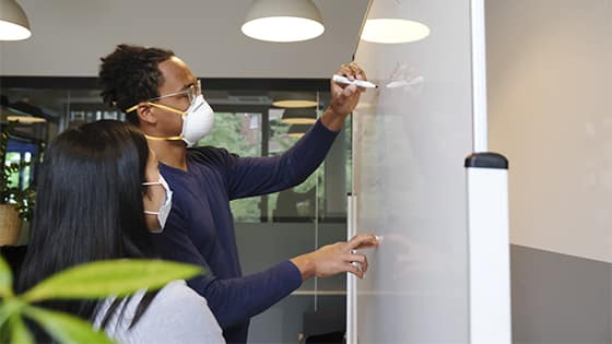 an African American man writes on a dry eraser board with an Asian woman; image used for blog post about not-for-profits teaming up for financial reporting
