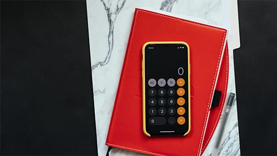a phone calculator sitting on top of a red journal and white and grey folder; image used for blog post about paying tax on social security benefits