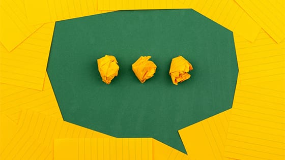 green and yellow paper forming a speech bubble with an ellipses; image used for blog post about easing not-for-profit staffers