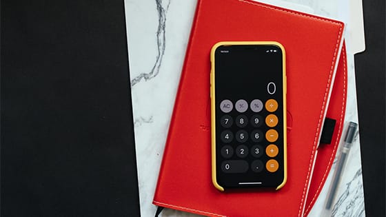 a phone calculator sitting on top of a red journal and white and grey folder; image used for blog post about IRA distribution rules