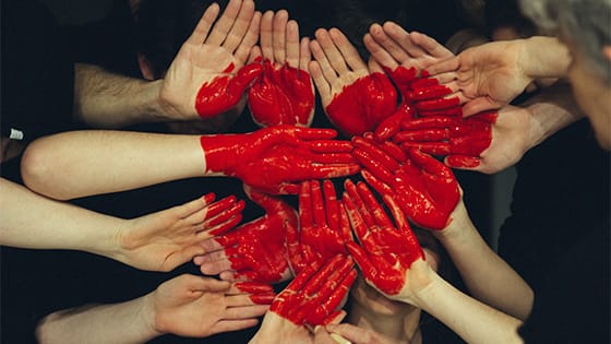 a collective of hands come together with red paint forming a heart; image used for blog post about not-for-profits collaborating on collective impact projects