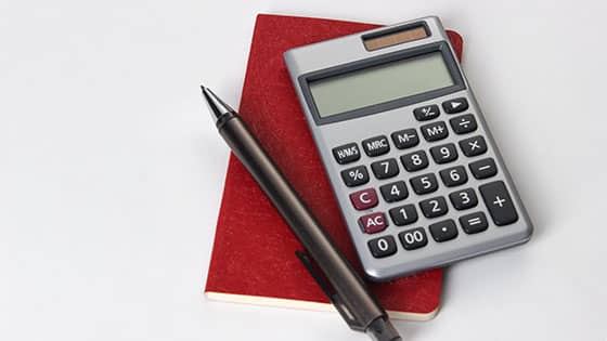 a calculator and a pen sitting on top of a red notebook; image used for blog post about accountable plans helping not-for-profit staff