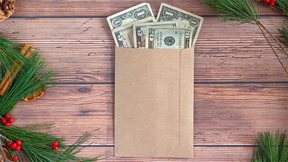 money bills in a brown envelope sitting on top of a wooden table with holly decorations; image used for blog post about annual exclusion for year-end gifts