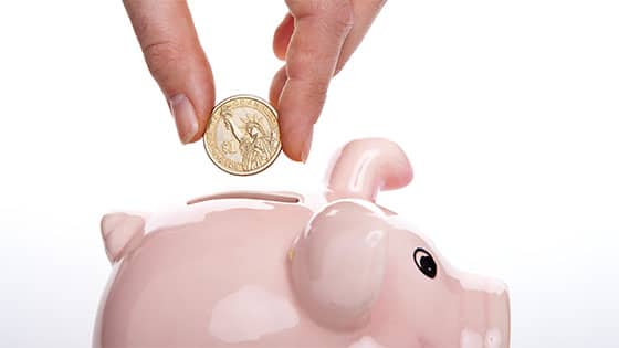 a person dropping a coin into a piggy bank; image used for blog post about student loan deduction qualifications