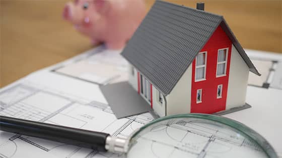 a magnifying glass and mini-model house and piggy bank sitting on top of real estate documents; image used for blog post about like-kind exchange deferring tax bill