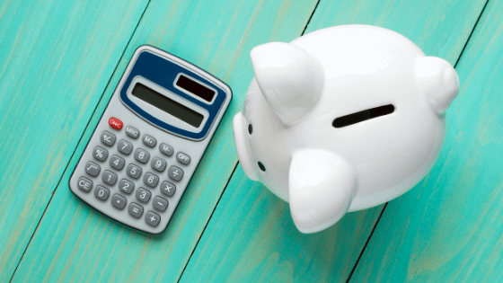 A hand-held calculator and ceramic piggy bank sitting on top of a wooden table; imaged used for blog post about tax implications of selling mutual fund shares