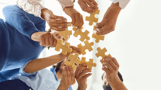 A photo of team members holding puzzle pieces together; image used for blog post about not-for-profits embracing accountability.