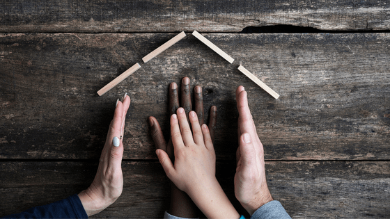 A photo of a mixed race family's hands forming a house; image used for blog post about adopting a child getting taxpayers benefits