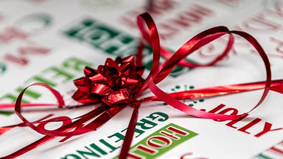 long shiny red ribbon tied tied on top of white wrapping paper with red and green holiday season messages, symbolizing gift tax rules