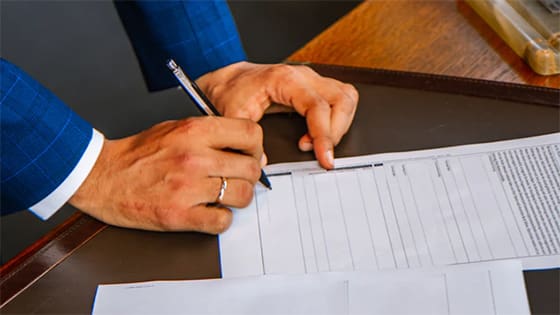 close up photo of a man in a blue suit, holding a pen to a paper, perhaps a document for a new rule from the Securities Exchange Commission (SEC)