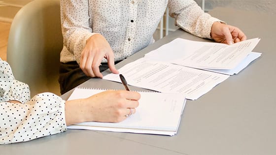 two women sitting at a table with various forms, one woman hands over a page and the other has pen in-hand to fill out paperwork; for a blog about not-for-profit board members information