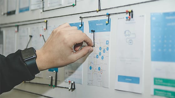 a man's hand putting a pin into a wall with several pieces of paper hung on a wall by black string and colored pins; used for a blog about restructuring not-for-profits