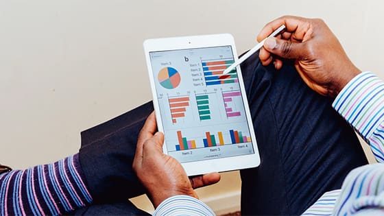 man holding a tablet with a pen looking at pie charts and bar graphs with statistical data; image used for blog post about tax rules for selling mutual funds