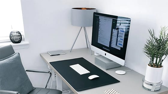 Large screen computer monitor sitting on a grey wooden desk in front of a computer rolling chair; image used for blog post about home office deductions