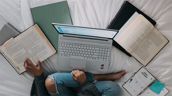girl sitting on her bed with a laptop and textbooks; image used for blog post about revised tax breaks for higher education