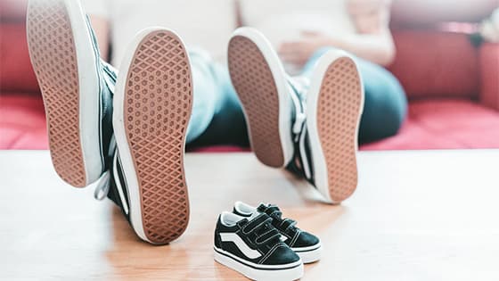 man and woman sitting on a couch with their shoes propped up on a coffee table with a pair of unworn baby tennis shoes; image used for blog post about parents child tax credit under American Rescue Plan Act