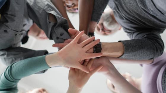 A group of people putting their hands in the middle to represent teamwork; image used for blog post about not-for-profit workers classified as employees