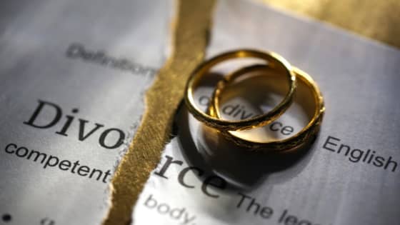 A photo of two wedding rings sitting on a ripped paper about divorce.