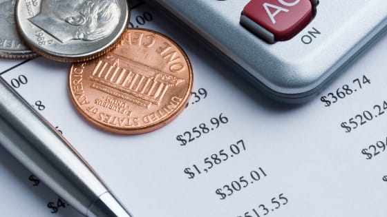 A photo of a calculator, coins, and pen sitting on top of financial documents; image used for blog post about not-for-profit spending policy