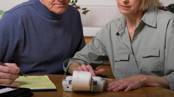 A photo of a married couple looking at printed paper of numbers on a calculator; image used for blog post about tax liabilities for spouses